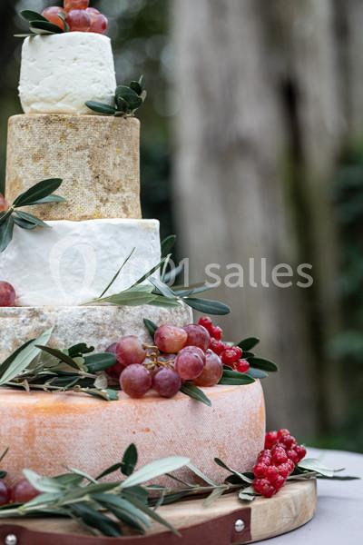 Tour de fromages empilés décorée de raisins rouges, baies rouges et feuilles d'olivier, sur un plateau en bois.