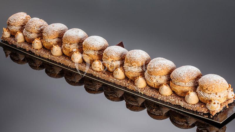 Dessert composé de choux garnis de crème pralinée, alignés sur une base croustillante, saupoudrés de sucre glace.