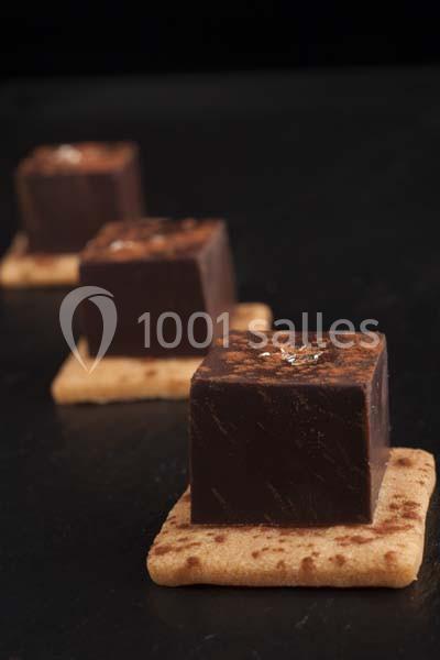 Carrés de chocolat posés sur des biscuits, décorés de poudre de cacao et d'une touche de feuille d'or.