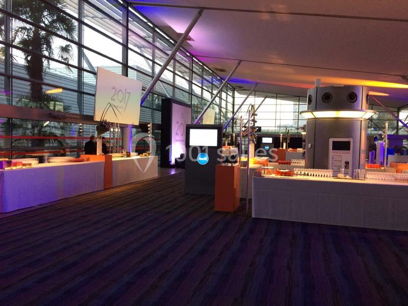 Salle d'exposition moderne avec stands lumineux, écrans et décorations, éclairée par une lumière tamisée.
