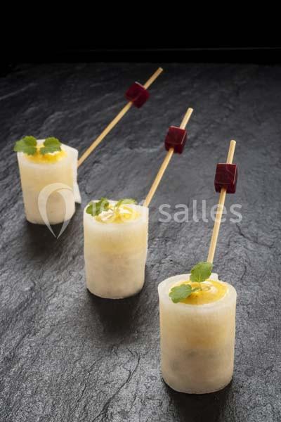 Bouchées de radis blanc garnies de sauce jaune, décorées de coriandre et accompagnées de cubes rouges sur brochettes.