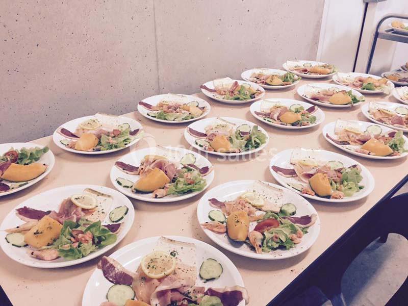 Assiettes dressées avec salade, charcuterie, fromage, tranches de melon et garnitures, alignées sur une table.