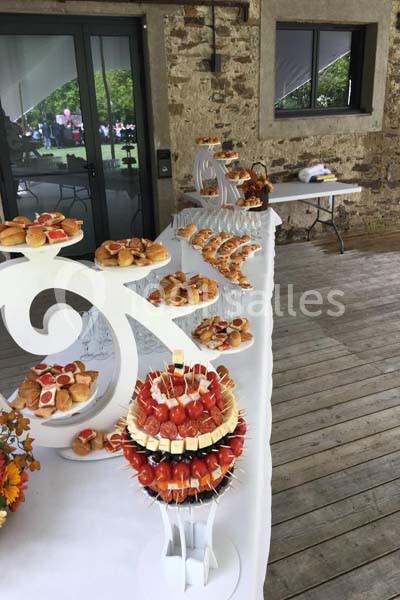 Buffet de réception avec des amuse-bouches variés disposés sur des présentoirs blancs dans un espace en bois et pierre.