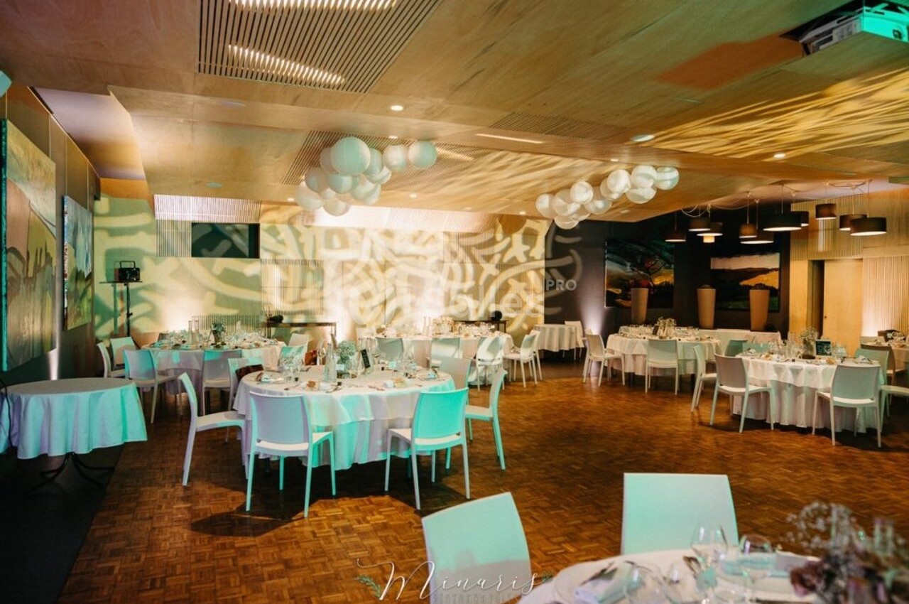 Salle de réception élégante avec tables dressées, éclairage tamisé et décorations suspendues.