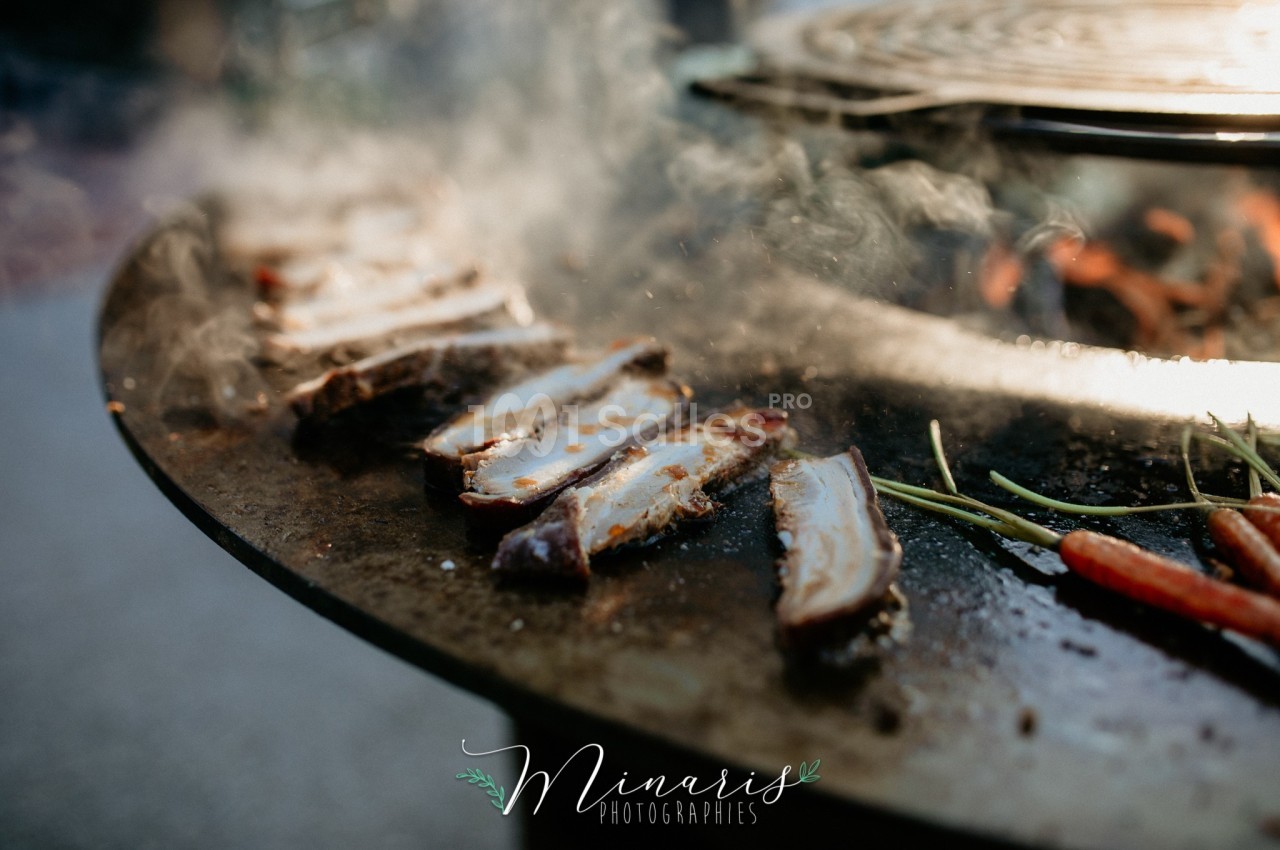 Tranches de viande grillées sur une plaque de cuisson avec des légumes, entourées de vapeur.