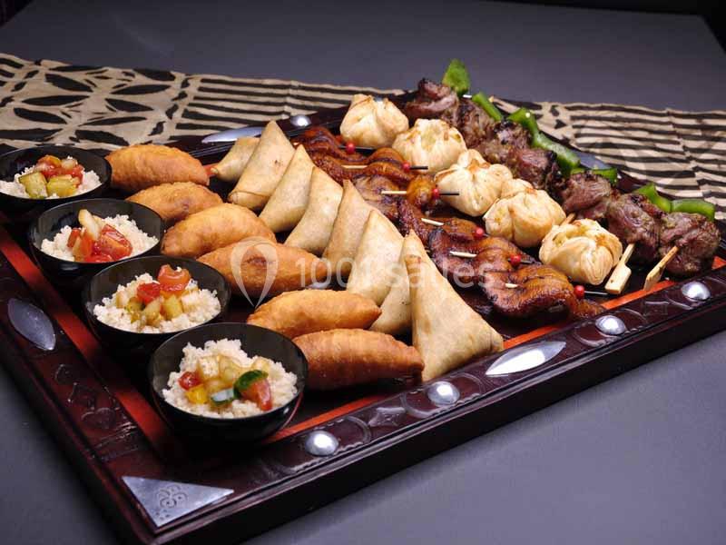 Plateau de spécialités variées comprenant samoussas, brochettes, beignets et bols de riz garnis.
