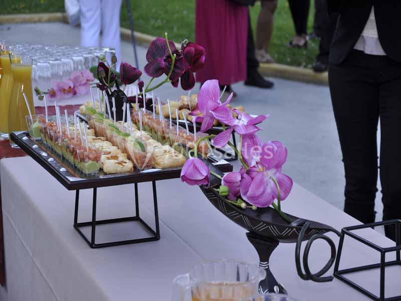 Buffet extérieur avec verrines, amuse-bouches et décorations florales sur une table dressée.