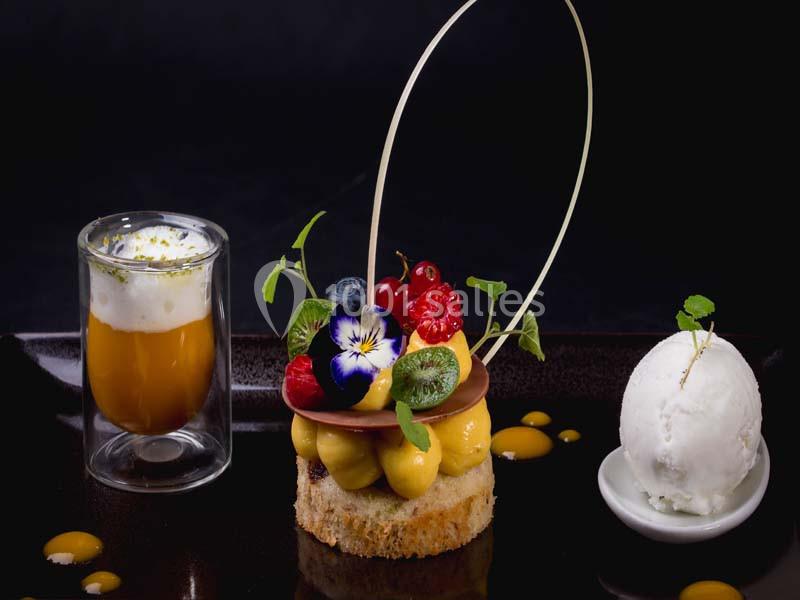 Dessert gastronomique composé d'un entremets aux fruits, d'une verrine et d'une boule de glace sur assiette noire.