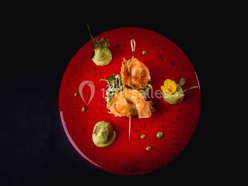 Assiette rouge avec présentation gastronomique de beignets dorés, purée verte, herbes fraîches et fleur comestible.