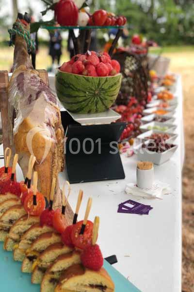 Buffet en plein air avec des tranches de pain garnies, un jambon entier, des fruits et des desserts disposés sur une table.