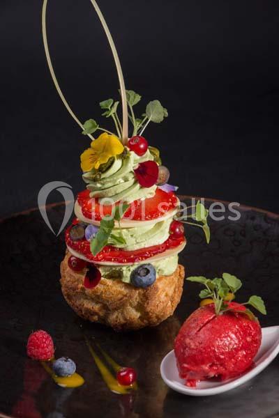 Pâtisserie garnie de crème verte, fruits rouges et fleurs comestibles, accompagnée d'une boule de sorbet rouge.