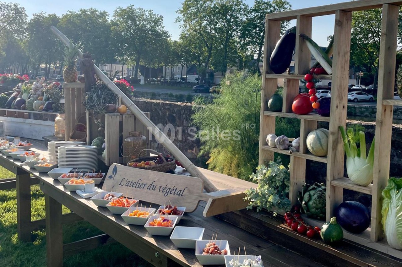 Buffet en plein air avec légumes frais, fruits et plats disposés sur une table en bois, entourée de verdure.