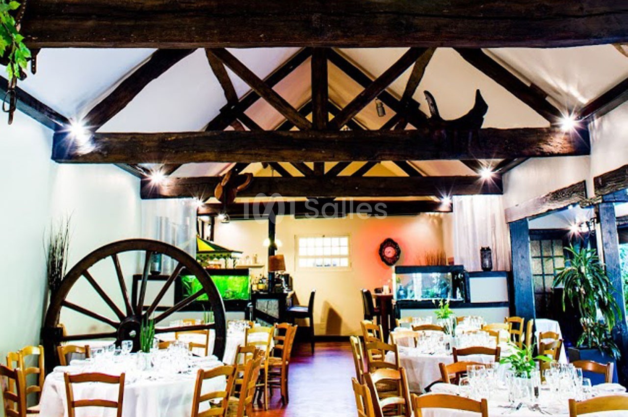 Salle de restaurant rustique avec poutres apparentes, tables dressées et décoration végétale.