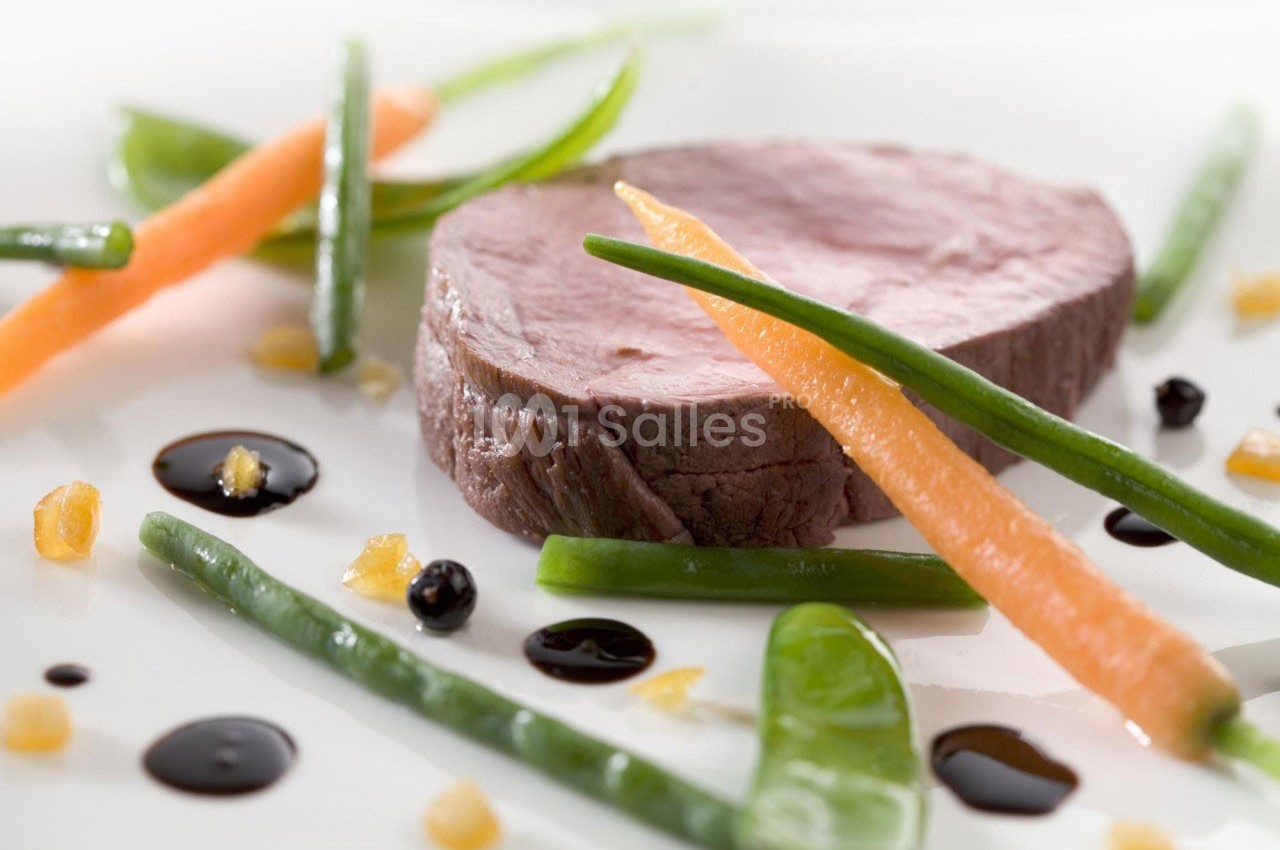 Tranche de viande cuite accompagnée de haricots verts, carottes et gouttes de sauce sur une assiette blanche.