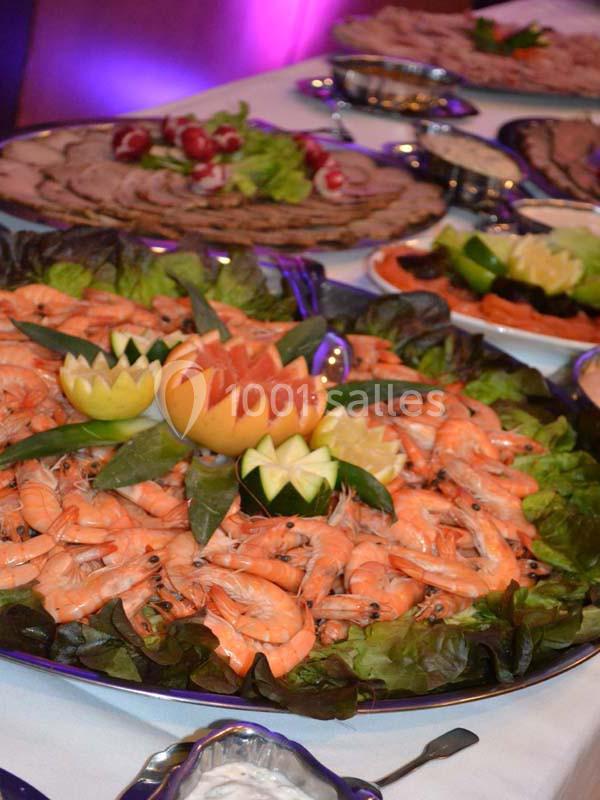 Plateau de crevettes entouré de feuilles de salade, décoré de fruits sculptés, sur une table de buffet.