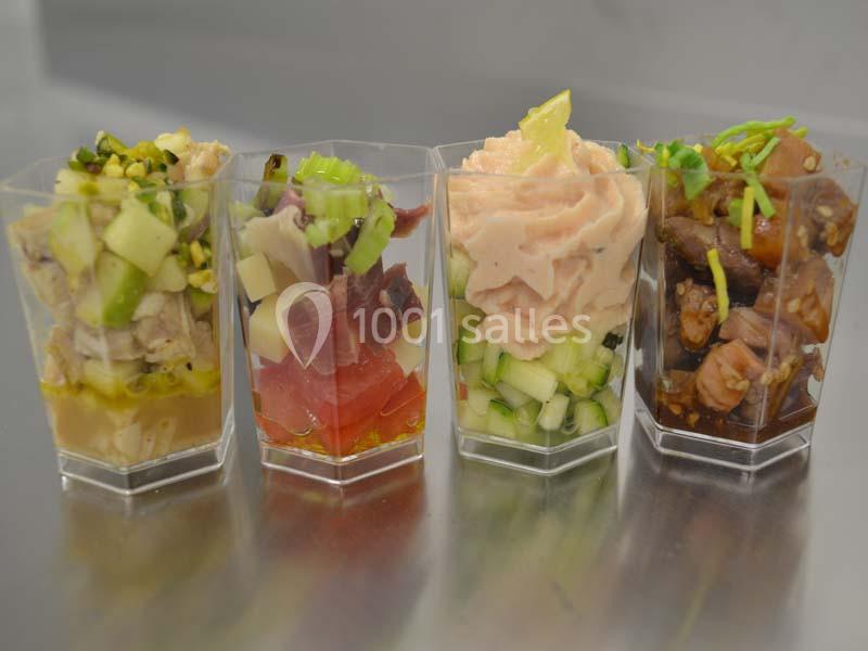 Quatre verrines contenant des préparations variées à base de légumes, poissons et condiments, présentées sur une surface…