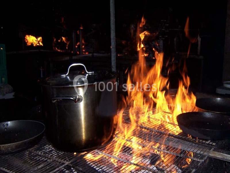 Une casserole en métal et des poêles sur un grill avec des flammes vives en arrière-plan.