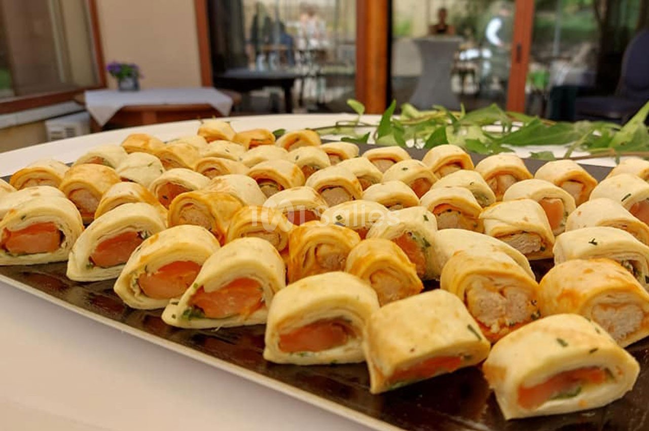Plateau de petits feuilletés garnis de saumon et de fromage, disposés sur une table lors d'un événement en extérieur.