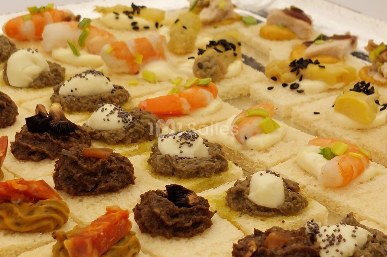 Plateau de canapés variés avec garnitures comme crevettes, tapenade, fromage et légumes sur pain blanc.