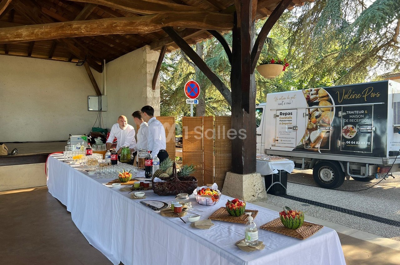 Table de buffet dressée sous un abri en bois, avec des plats variés et un camion de traiteur stationné à proximité.