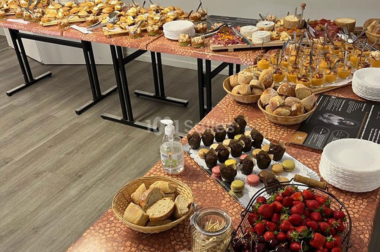 Buffet varié avec viennoiseries, fruits, desserts, pains et condiments disposés sur des tables dans une salle.