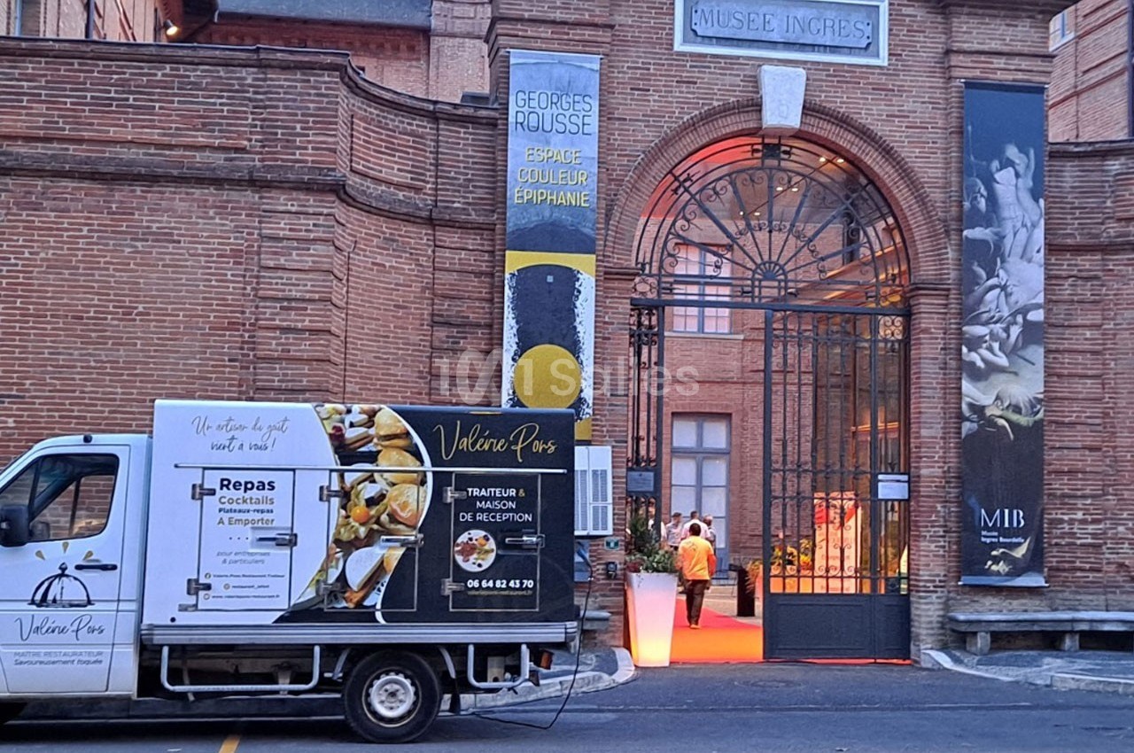 Camion de traiteur stationné devant l'entrée éclairée du musée Ingres à Montauban, avec des affiches visibles.