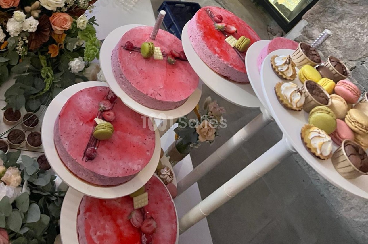 Desserts variés sur des présentoirs, incluant des entremets roses, macarons colorés et tartelettes décorées.