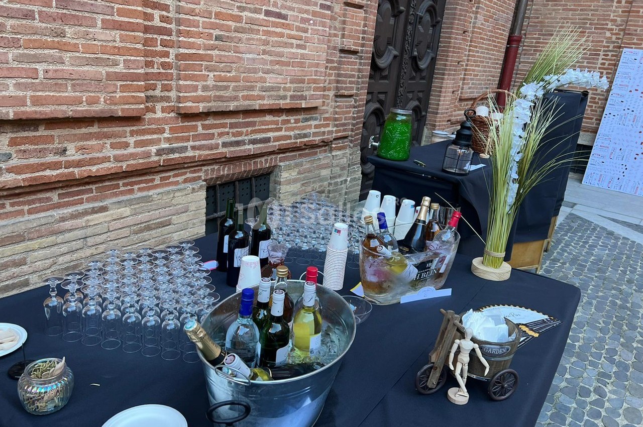 Table de réception en extérieur avec boissons, verres, seau à glace et décoration sur fond de mur en briques.