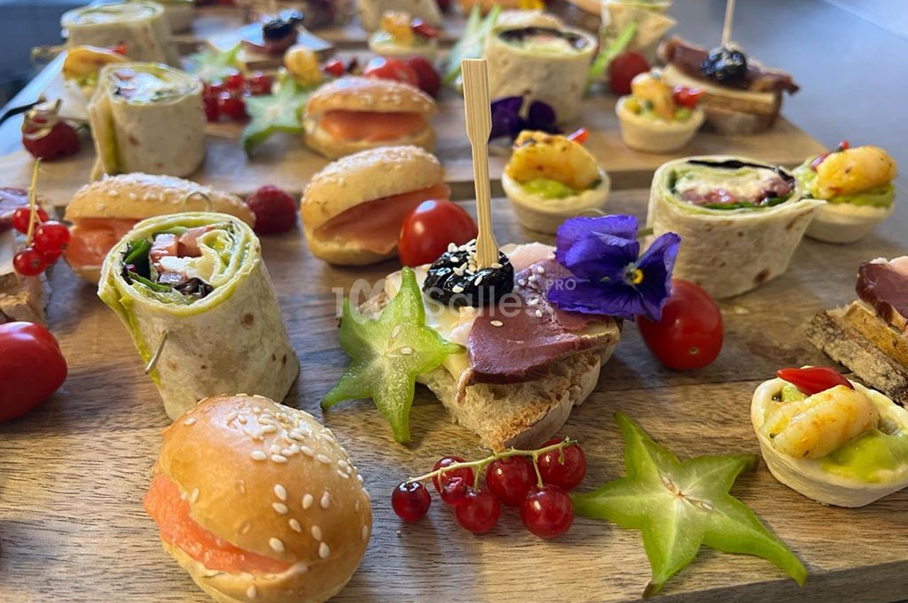 Plateau de bouchées variées comprenant wraps, mini-sandwichs, fruits et garnitures colorées sur une planche en bois.