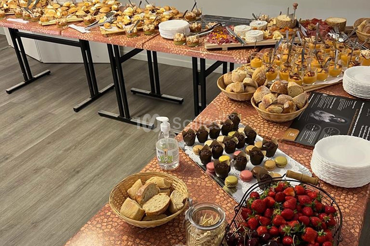Buffet varié avec viennoiseries, fruits, desserts, pains et condiments disposés sur des tables dans une salle.