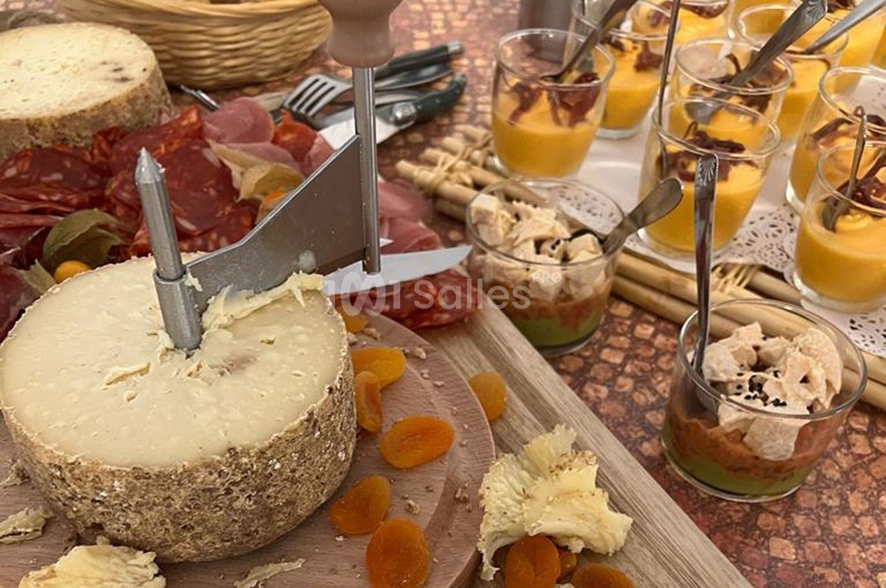 Plateau avec fromage à pâte dure tranché, charcuterie, abricots secs et verrines de mousse salée garnie.