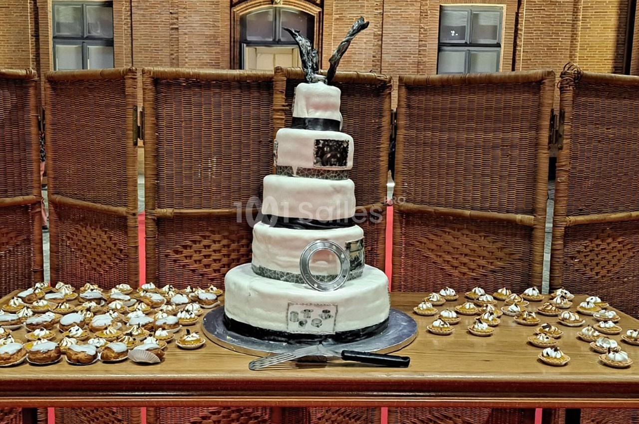 Gâteau de mariage à plusieurs étages décoré de noir et blanc, entouré de petites pâtisseries sur une table en bois.