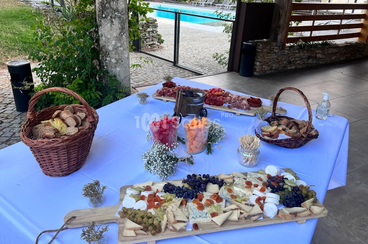 Table dressée avec des planches de fromages, fruits et charcuteries, paniers de pain, près d'une piscine en extérieur.