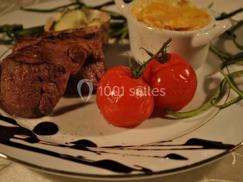 Assiette avec filet de viande, tomates cerises rôties, gratin en cocotte et décoration de sauce balsamique.
