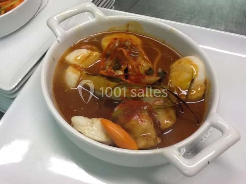 Bol de soupe avec raviolis, légumes variés et bouillon brun, servi dans un plat en céramique blanche.