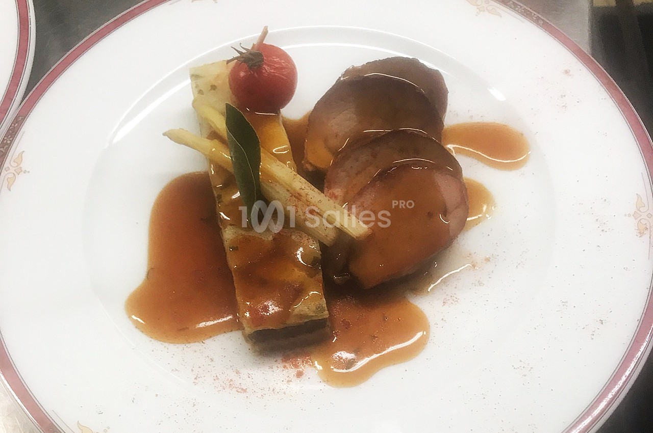 Assiette gastronomique avec viande nappée de sauce, accompagnée de légumes et d'un flan salé, décorée d'une tomate cerise.