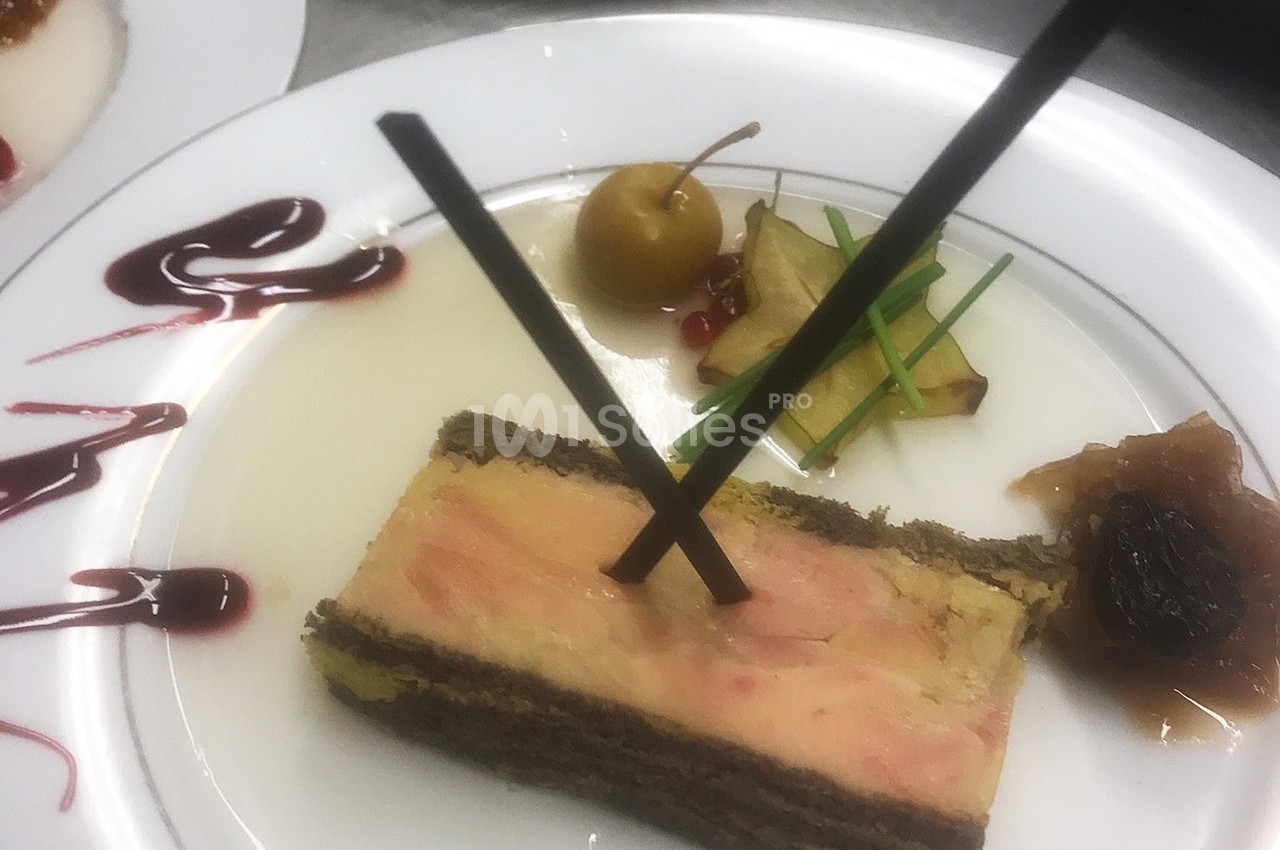 Tranche de foie gras sur assiette avec décorations de fruits, sauce et garnitures élégantes.