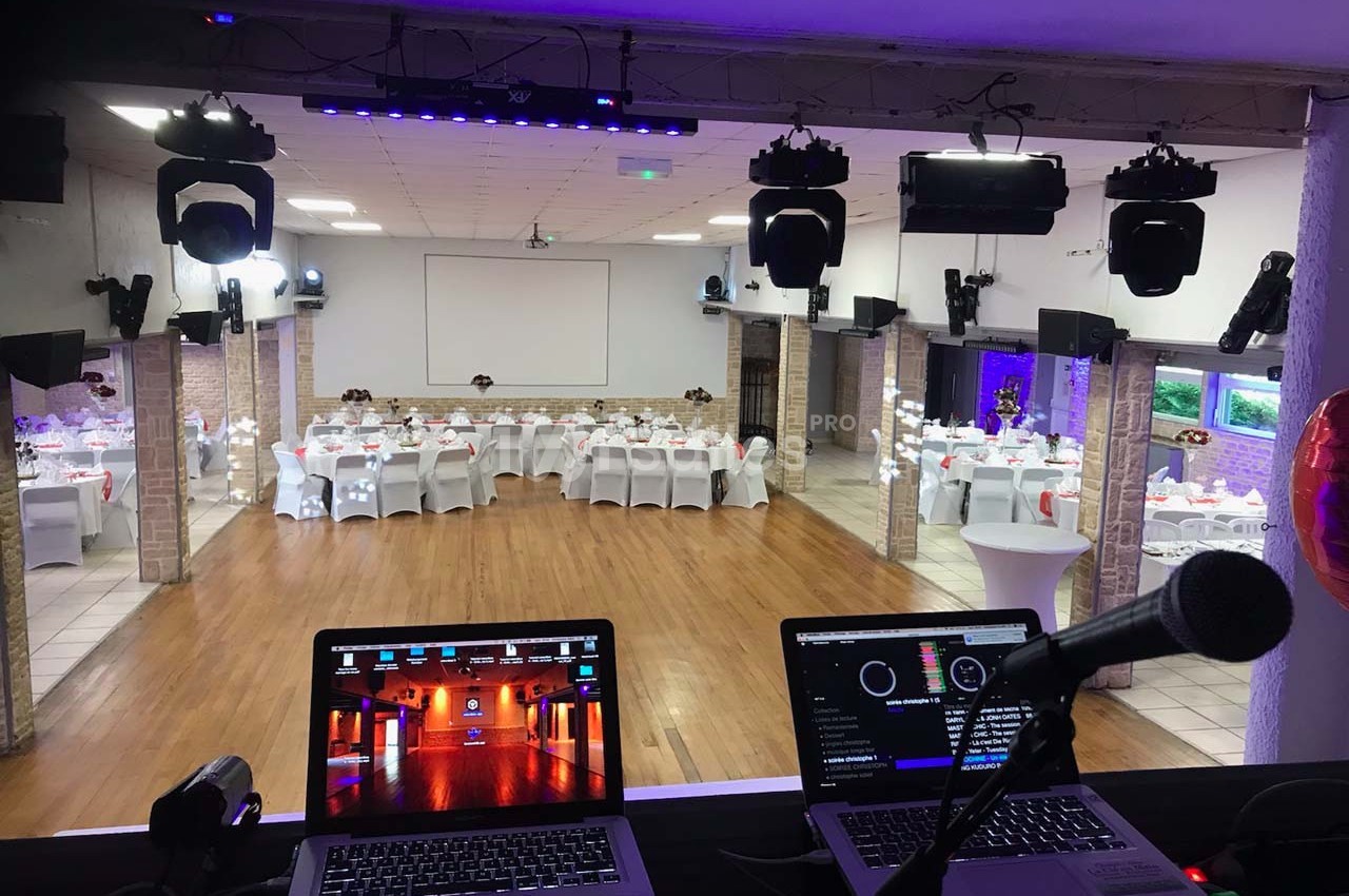 Salle de réception décorée avec tables dressées, vue depuis une régie équipée d'ordinateurs et d'un micro.