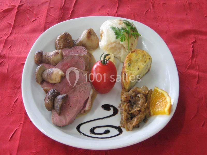 Assiette garnie de viande, champignons, tomate, purée, tranche d'orange, oignons confits et sauce décorative.