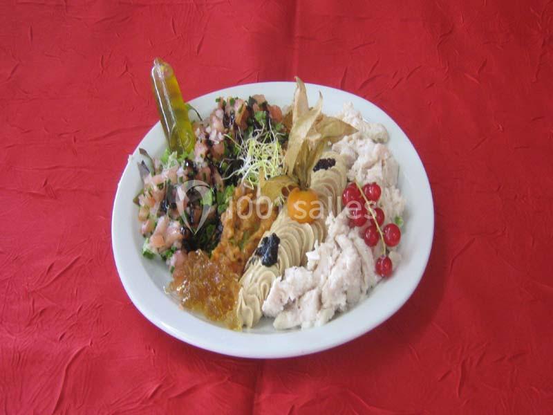 Assiette garnie de tartinades, crudités, fruits décoratifs et condiments sur une nappe rouge.