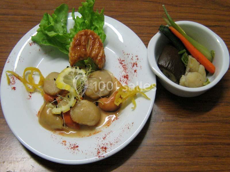 Assiette de noix de Saint-Jacques avec sauce et garniture de légumes, accompagnée d'un bol de légumes vapeur.