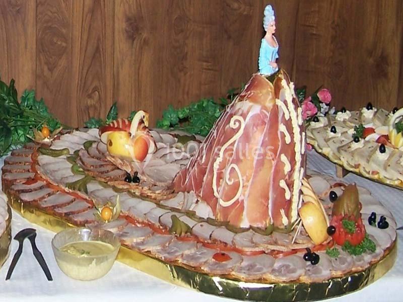 Plateau décoratif de charcuterie avec tranches de viande, légumes, fruits sculptés et une figurine en haut d'une structure.