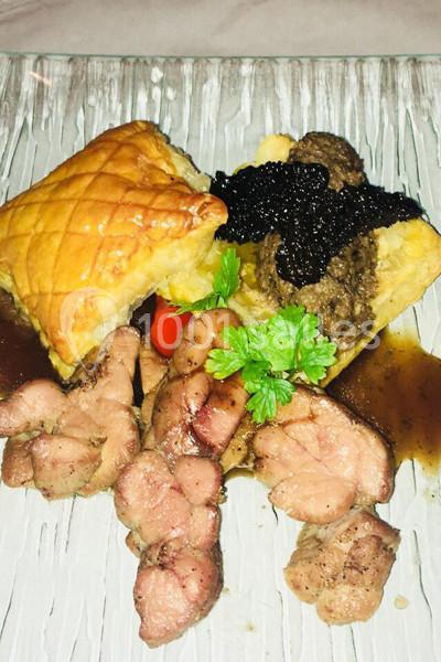 Assiette composée de viande grillée, feuilleté doré, purée garnie de sauce et herbes fraîches.