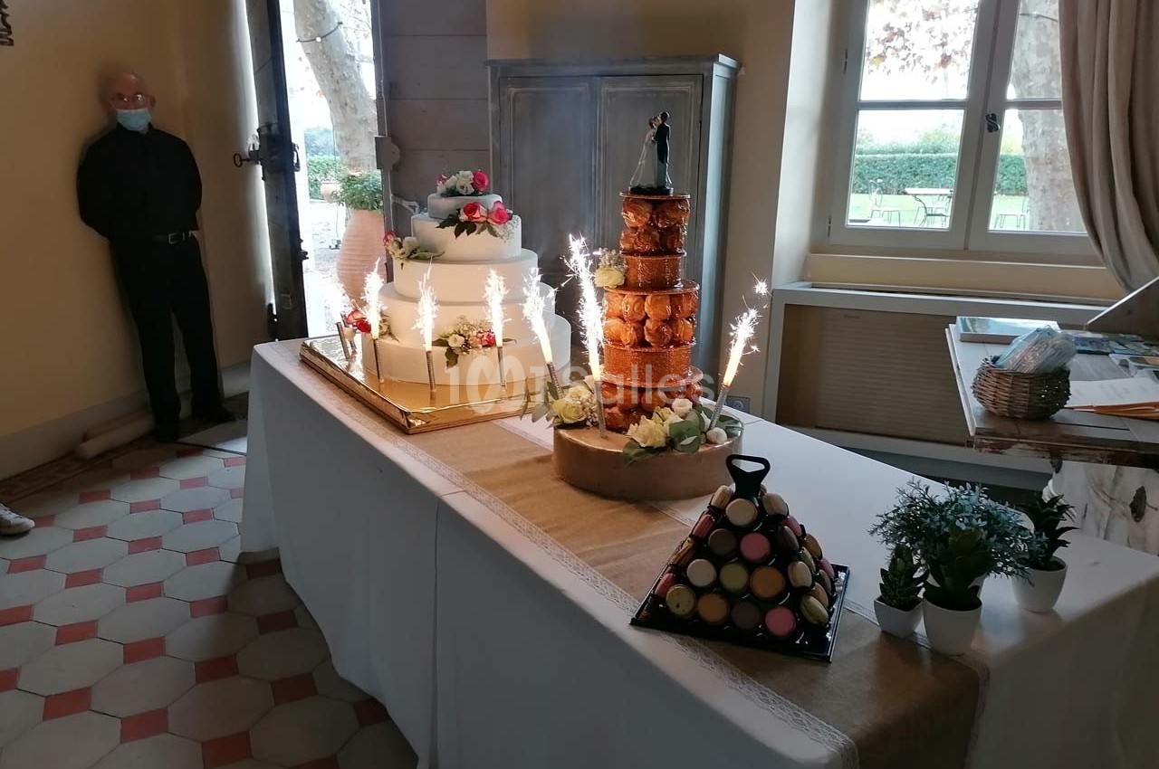 Table de desserts de mariage avec pièce montée, croquembouche, macarons et décorations florales, entourée de bougies…