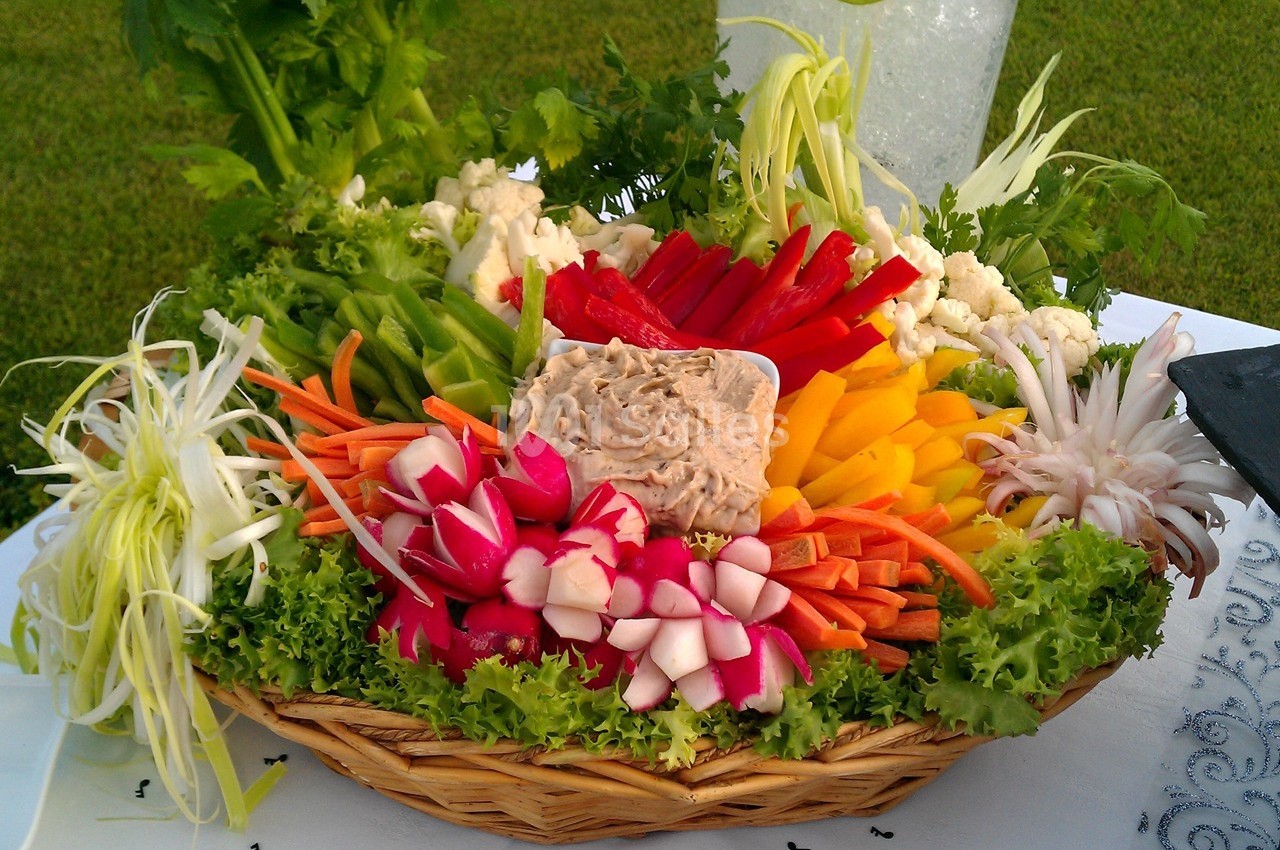 Plateau de crudités colorées avec radis, carottes, poivrons, chou-fleur et trempette au centre, présenté sur un lit de…