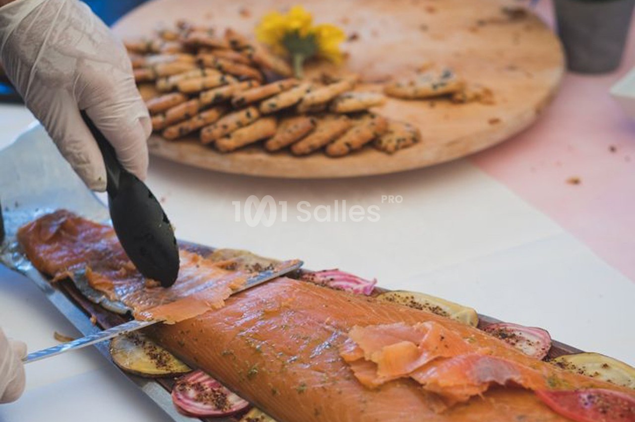 Préparation de tranches de saumon fumé sur un plateau garni de légumes, avec des biscuits apéritifs en arrière-plan.