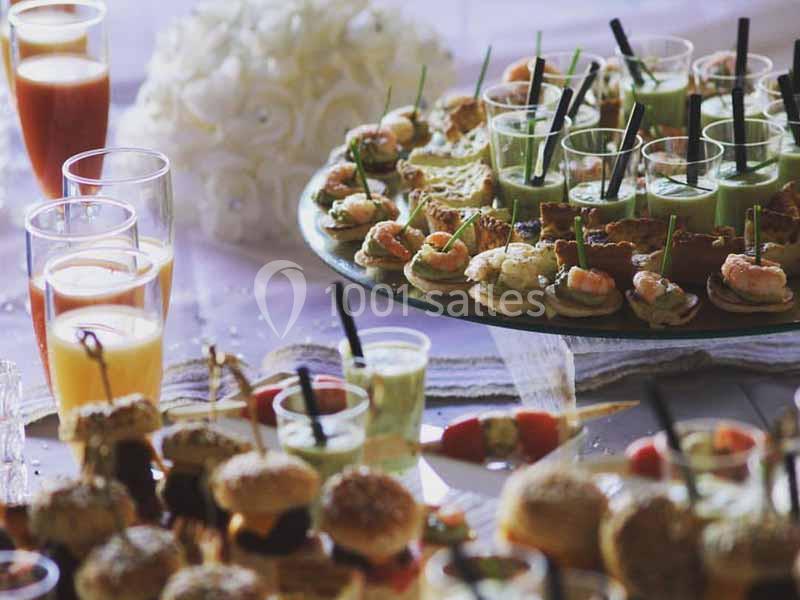 Plateau de bouchées apéritives variées avec verrines, mini-sandwichs et brochettes, entouré de boissons.