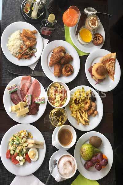 Assortiment varié de plats sur une table, incluant fruits, viennoiseries, salades, boissons et plats chauds.