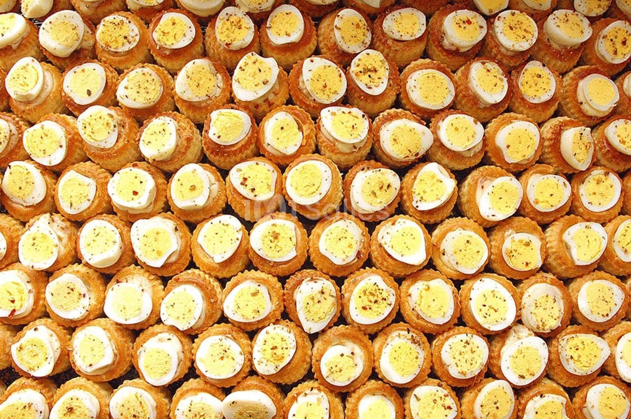 Assortiment de bouchées garnies d'œufs durs tranchés et saupoudrées d'épices, disposées en rangées serrées.