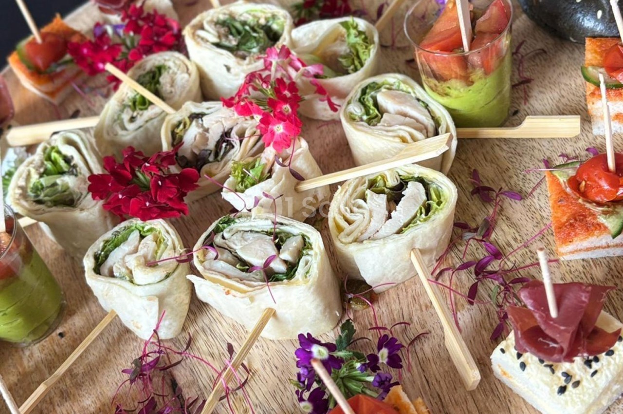 Plateau de wraps garnis de légumes et de viande, accompagnés de verrines et bouchées décorées de fleurs comestibles.